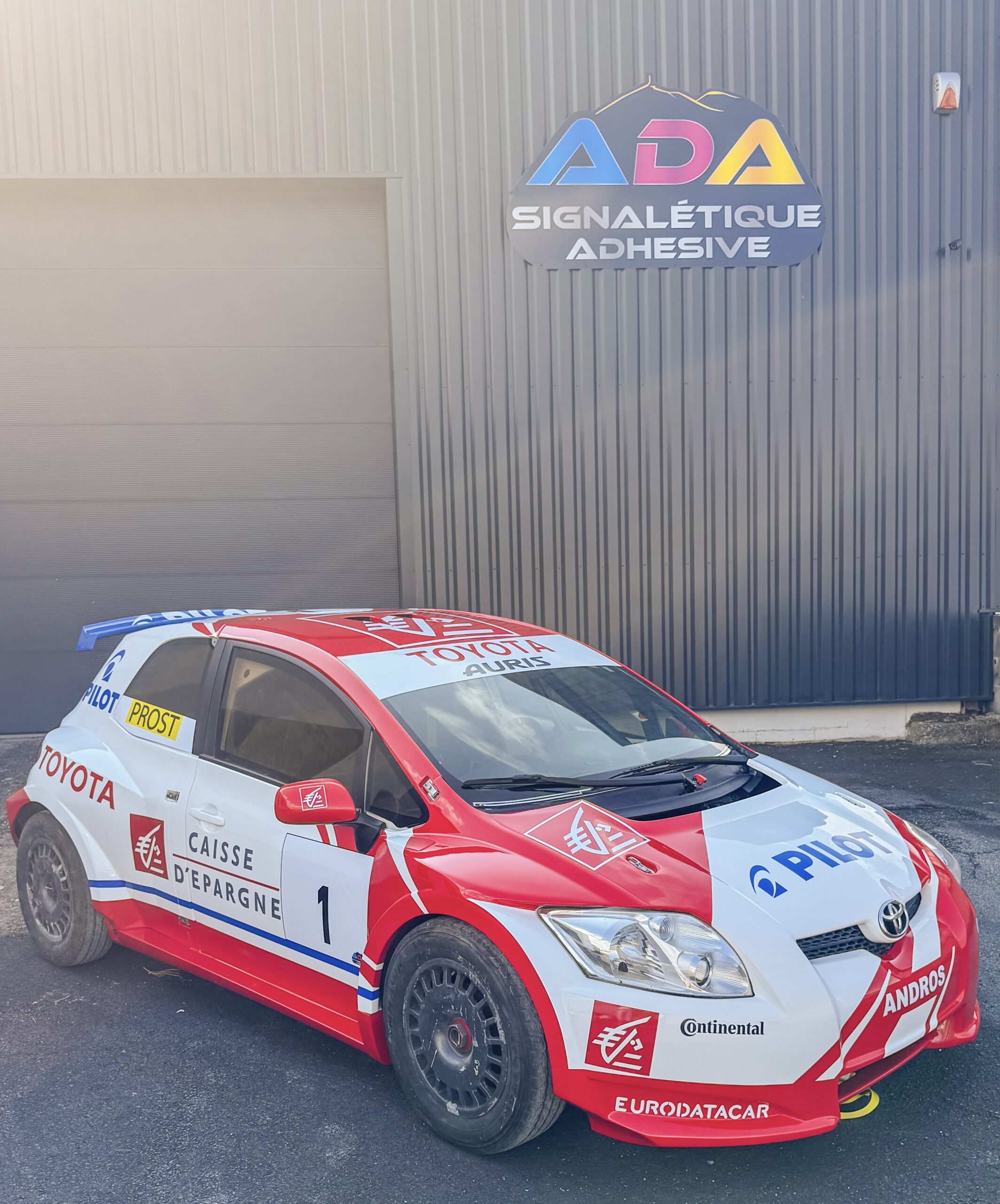 Toyota Auris de compétition du Trophée Andros décorée aux couleurs d’Alain Prost devant l’atelier ADA Signalétique à Lempdes