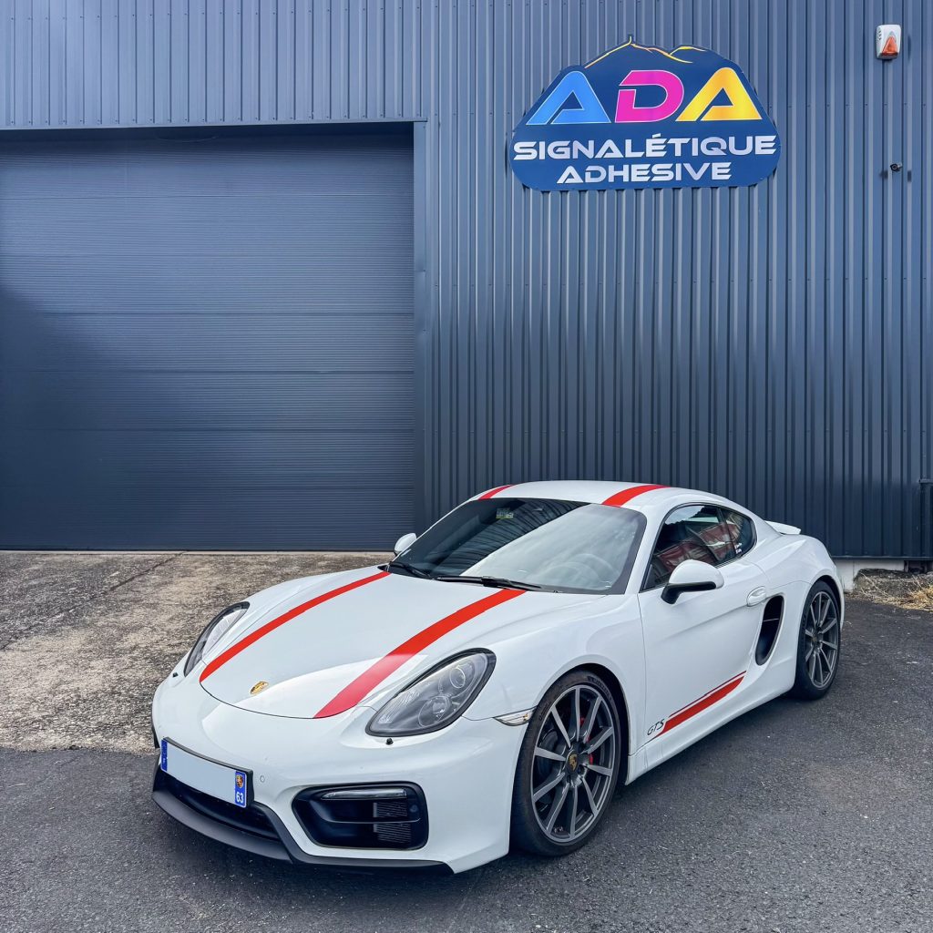 Porsche Cayman GTS blanche personnalisée avec bandes rouges devant ADA Signalétique à Clermont-Ferrand